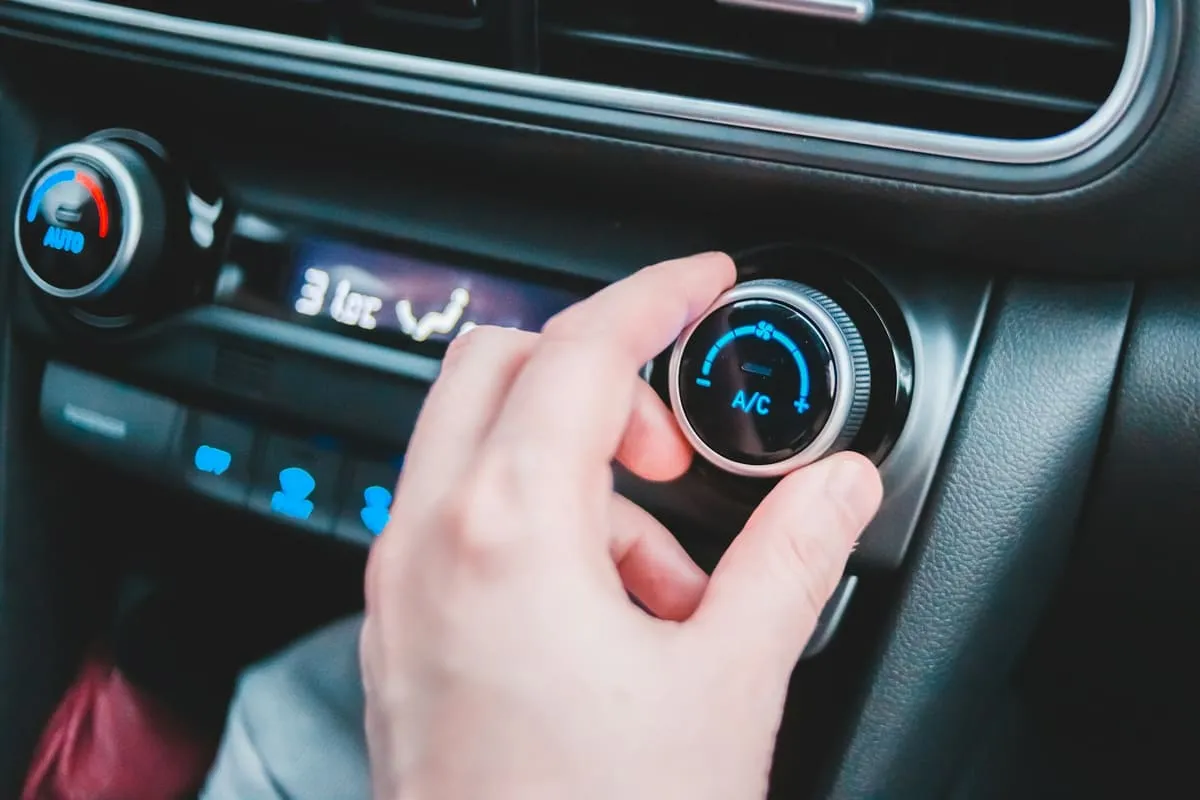 Dłoń na pokrętle klimatyzacji z podświetlonym na niebiesko przyciskiem A/C