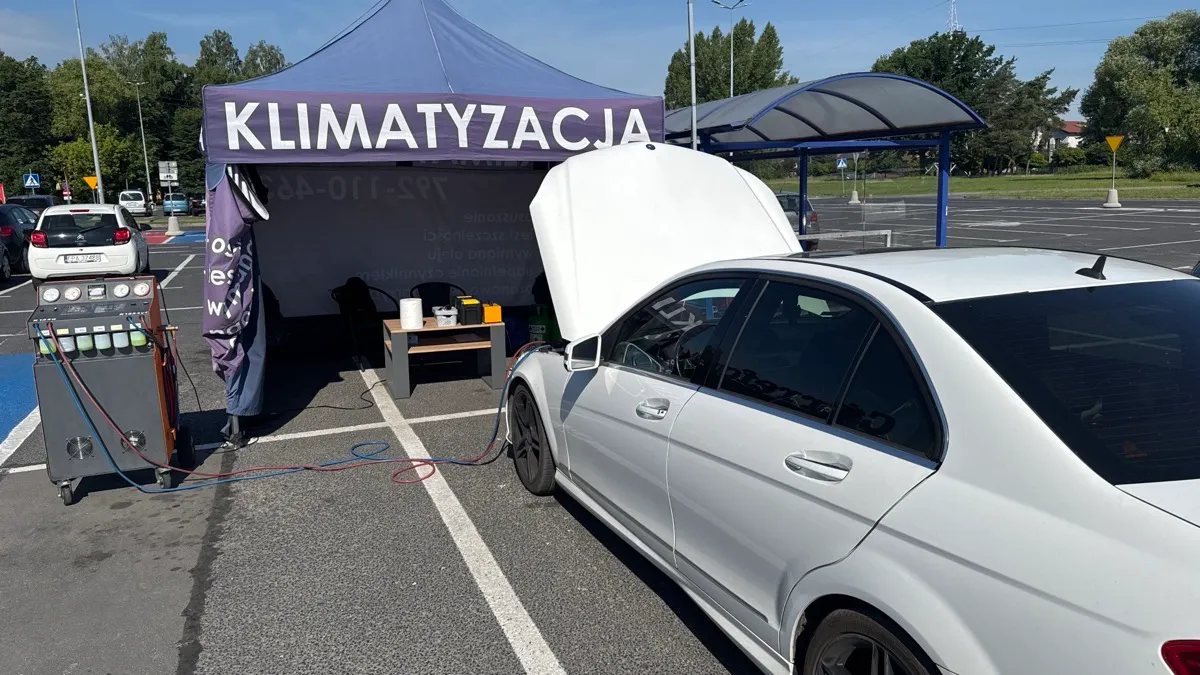 Białe auto z otwartą maską podłączone do stacji serwisowej klimatyzacji na parkingu w słoneczny letni dzień