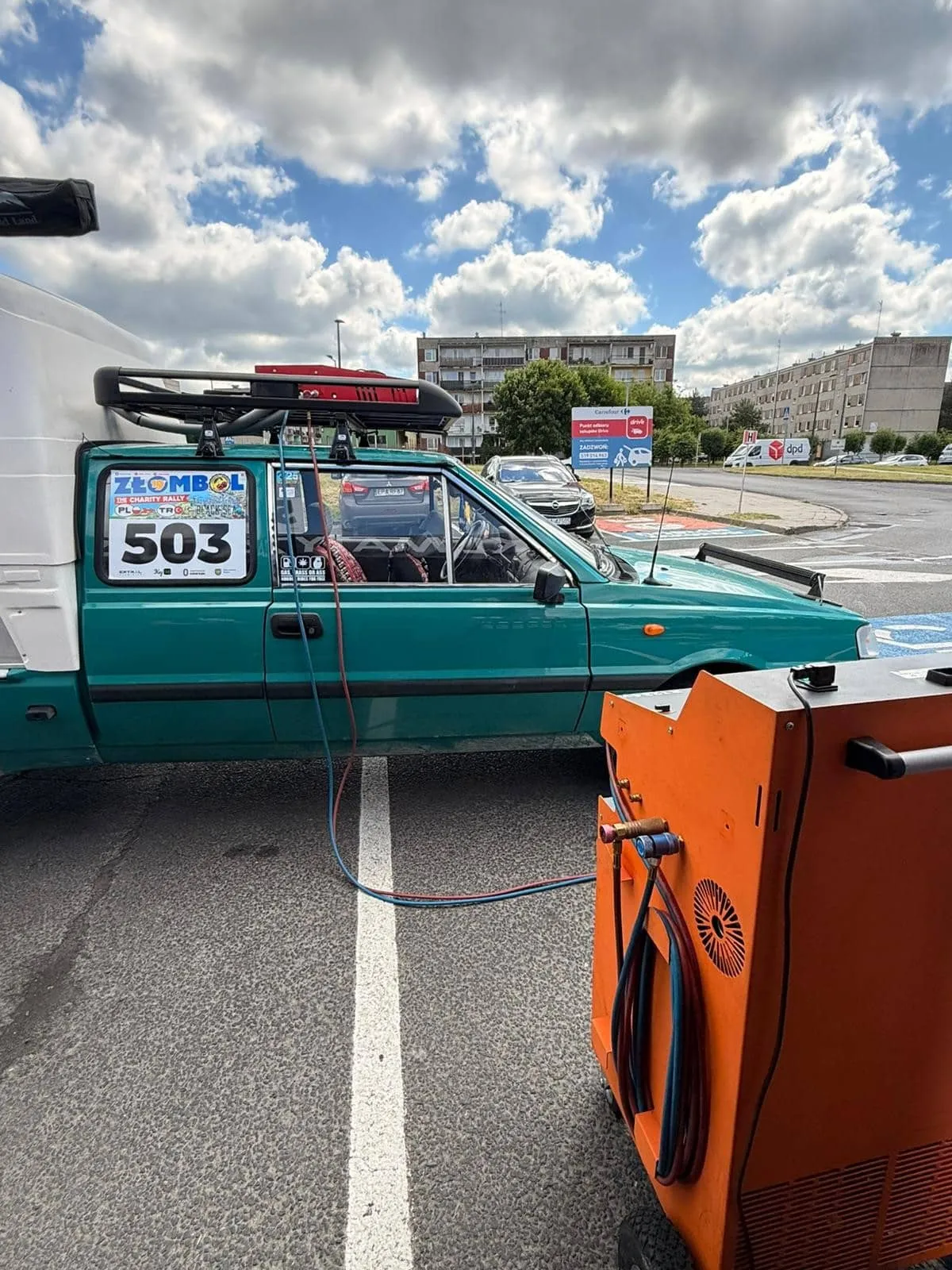 Serwis klimatyzacji na parkingu Carrefour w Pabianicach, w tle bloki i market