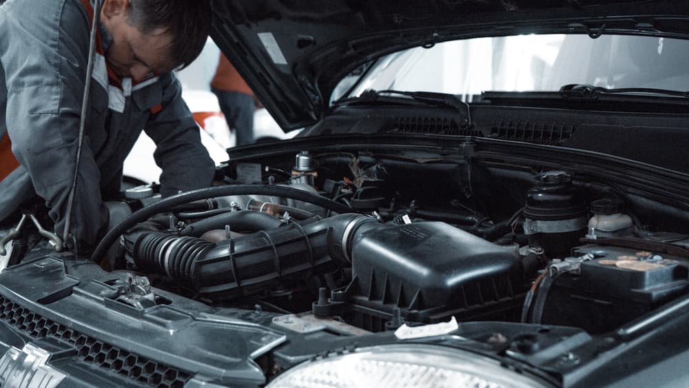 Mechanik pochylony nad komorą silnika podczas serwisu klimatyzacji