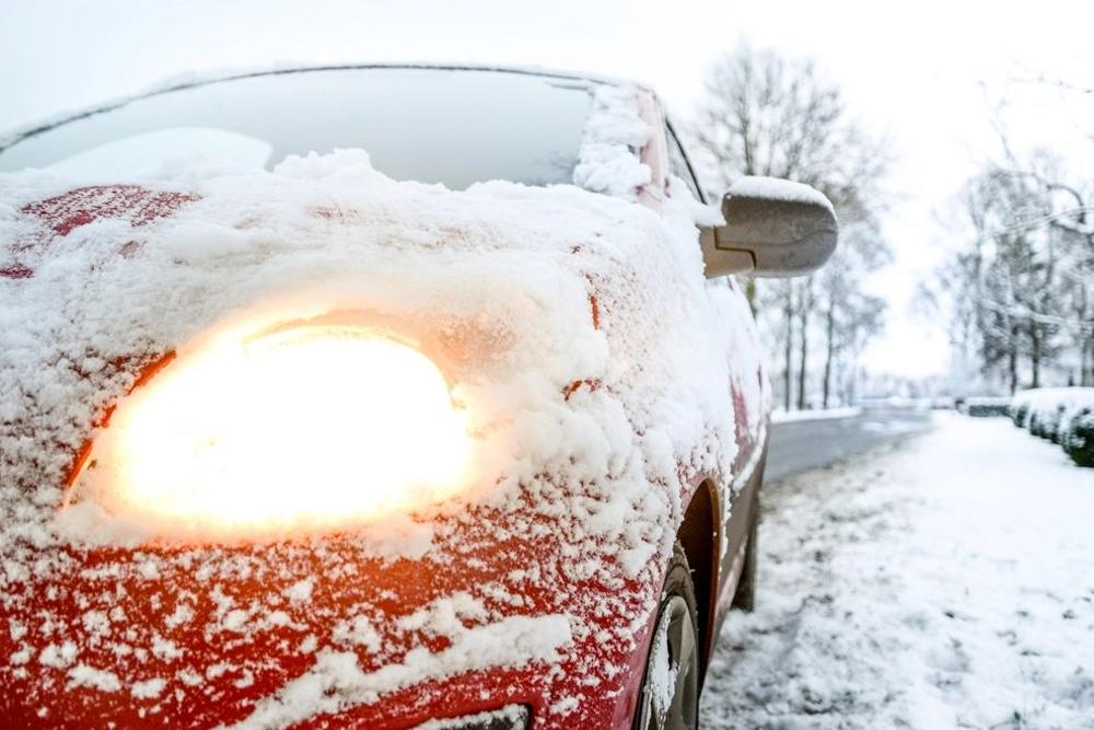 Zaśnieżone auto z zapalonymi światłami na zimowej drodze