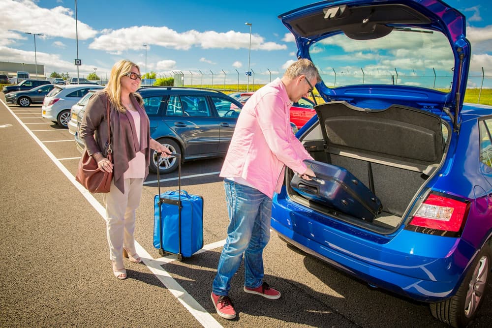 Rodzina pakuje walizki do bagażnika auta na parkingu przed podróżą